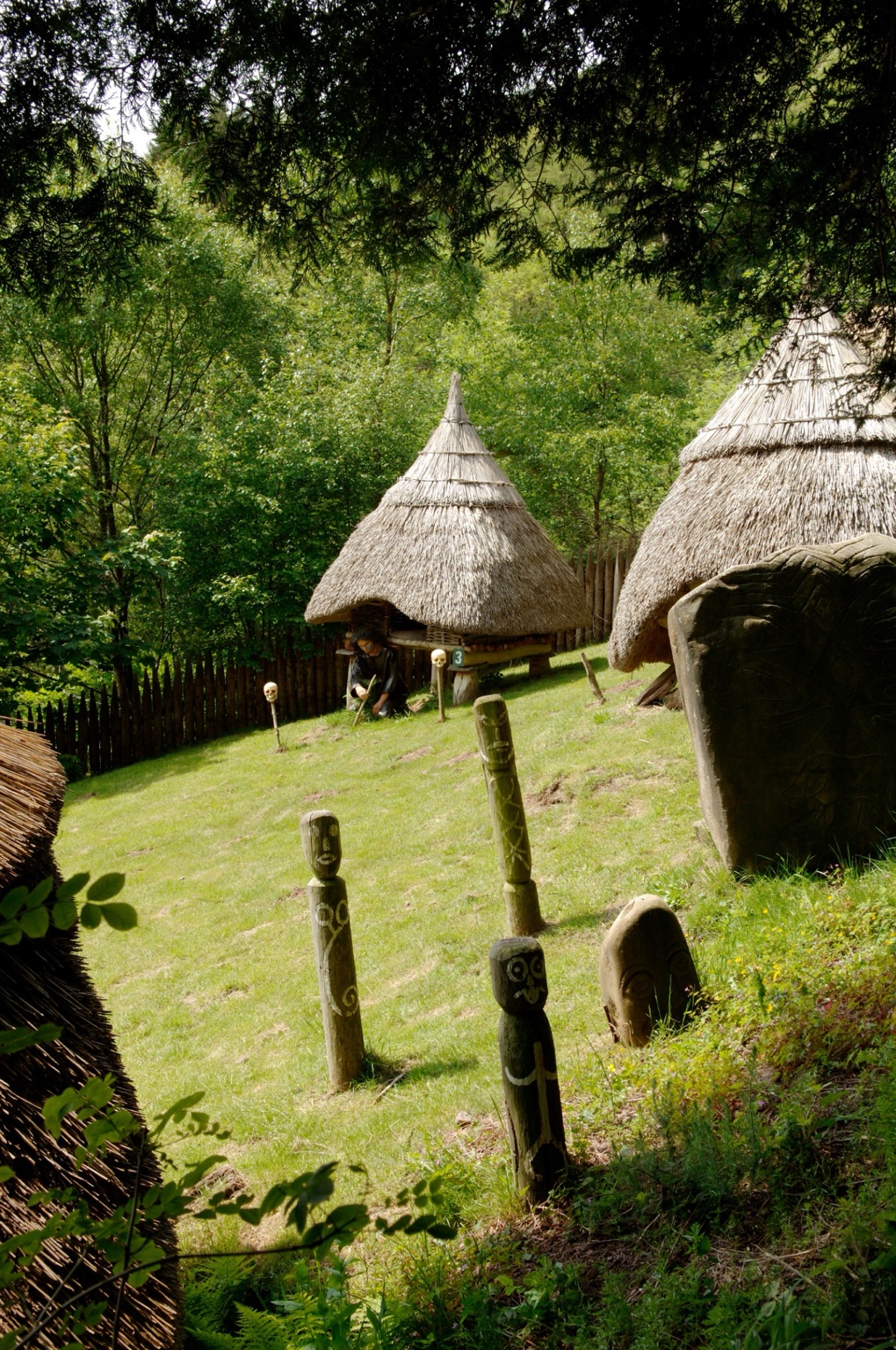 Reconstructed thatched roundhouses and carved wooden figures at the Iron Age Village, Dan-yr-Ogof