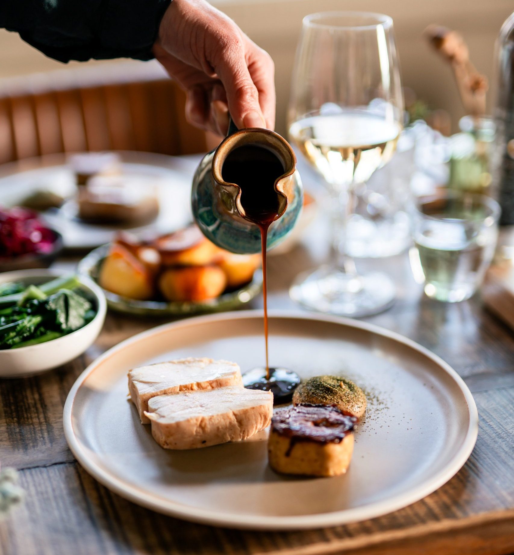 a hand pouring a jus from a jug onto a plate of food