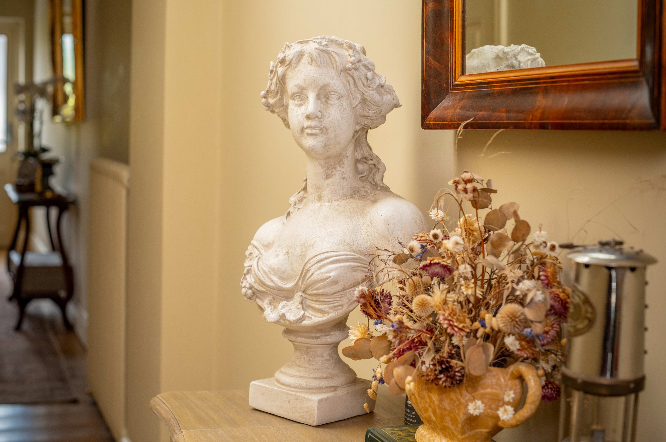 an antique bust on a tabel in teh hall, a vase of dried flowers