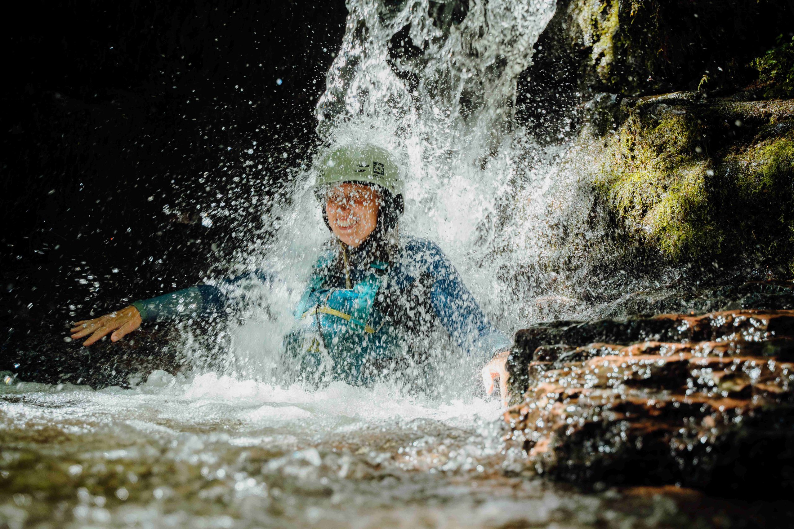 a smiling person standing under a waterfall
