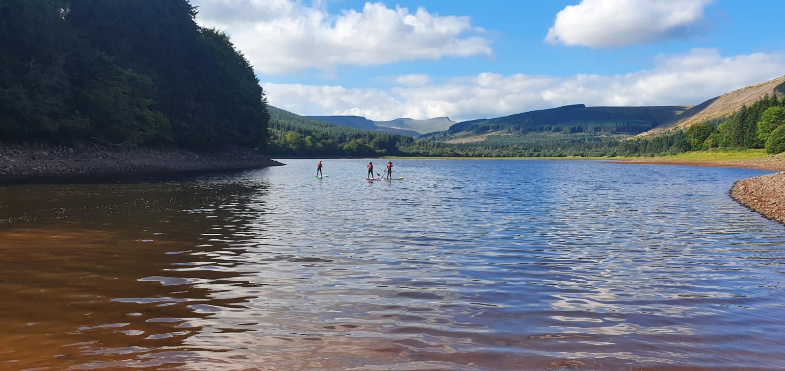 a view of SUP users with the central Beacons ridgeline in the distance.
