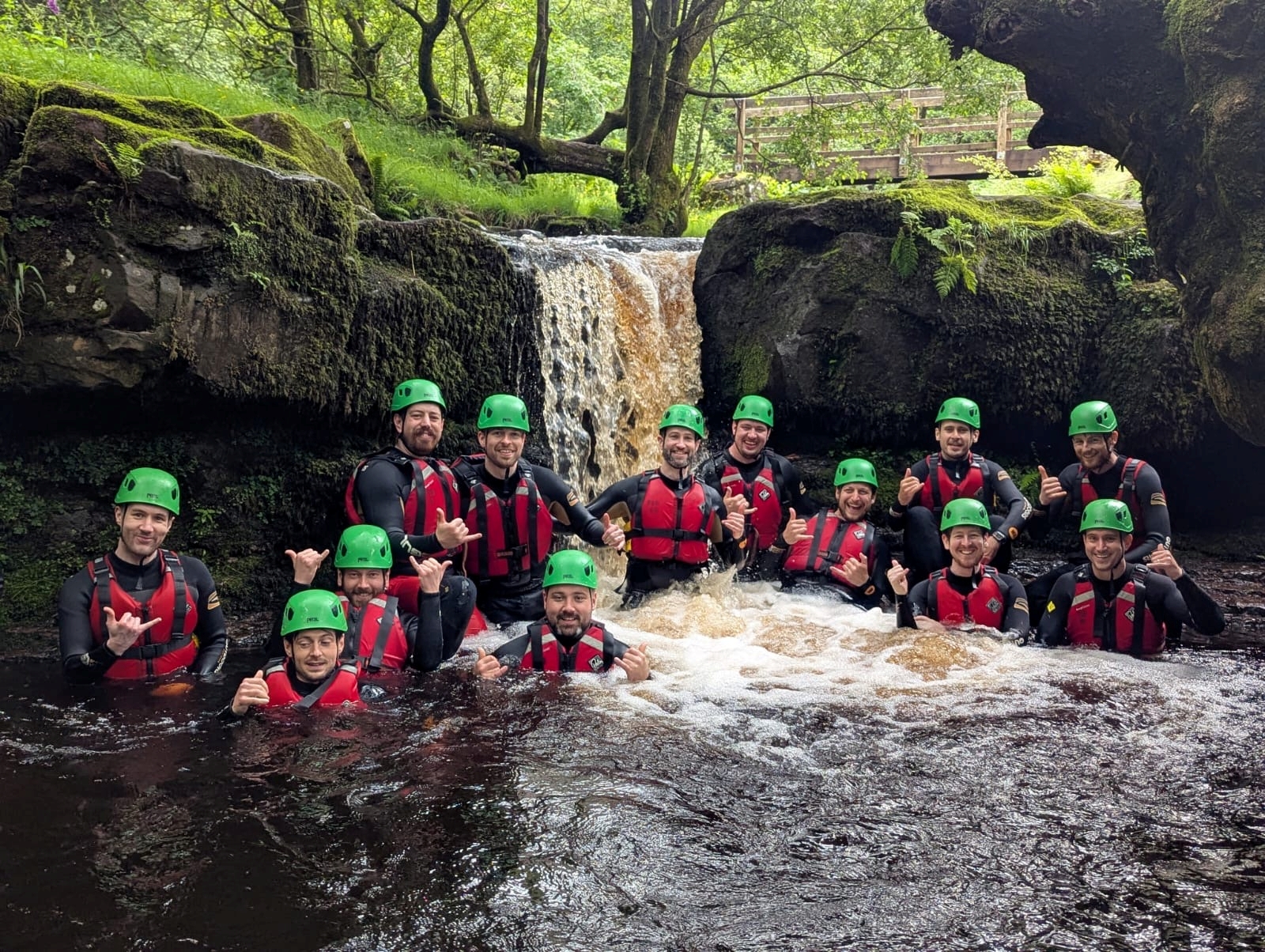 a group of adults and children jumping into a river by a waterfall. All in full safety kit