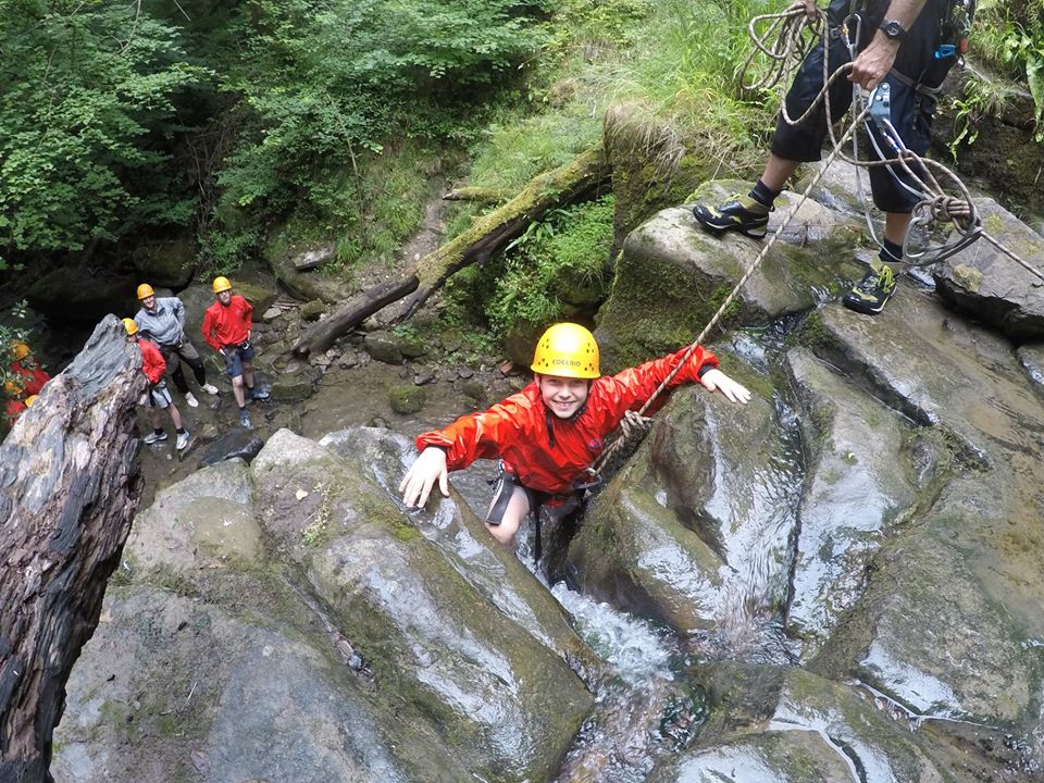 Participant climbing natural rock face with instructor support.