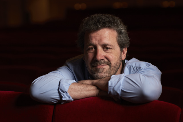 Theatre director Dominic Dromgoole leaning on the back of a red theatre seat