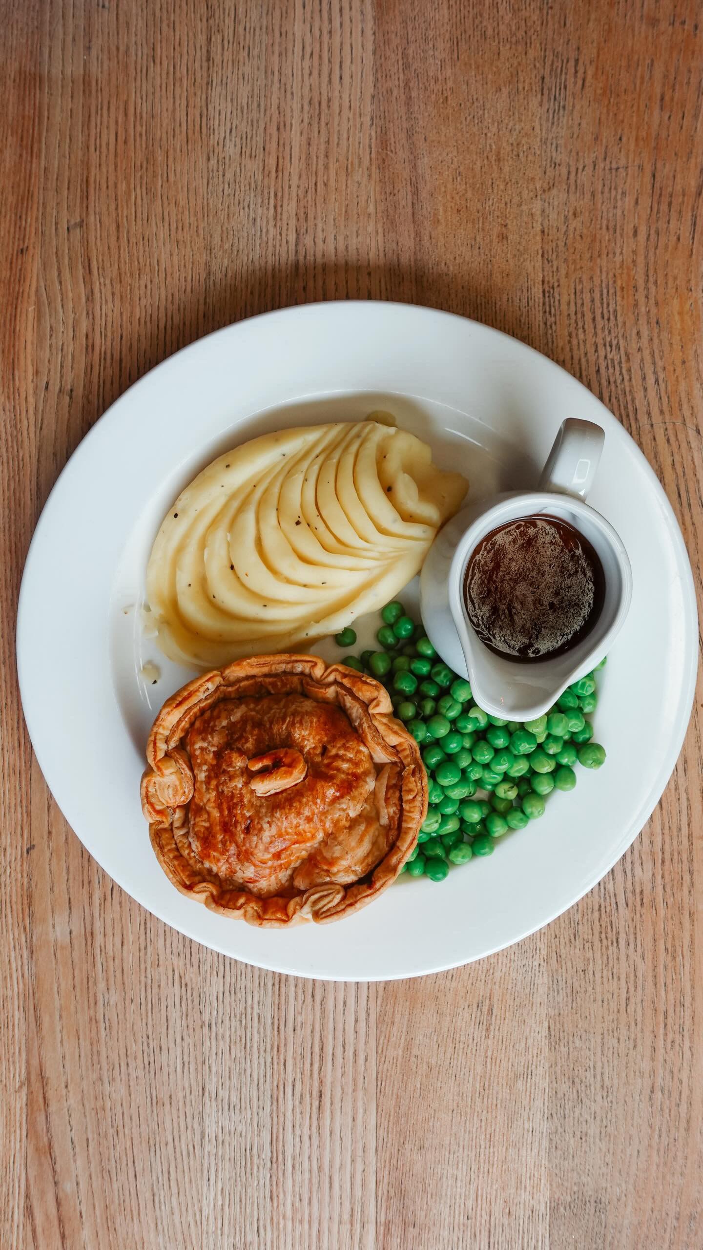 “Individual pie served with mashed potatoes, green peas and gravy on a white plate at Brecon Tap.”
