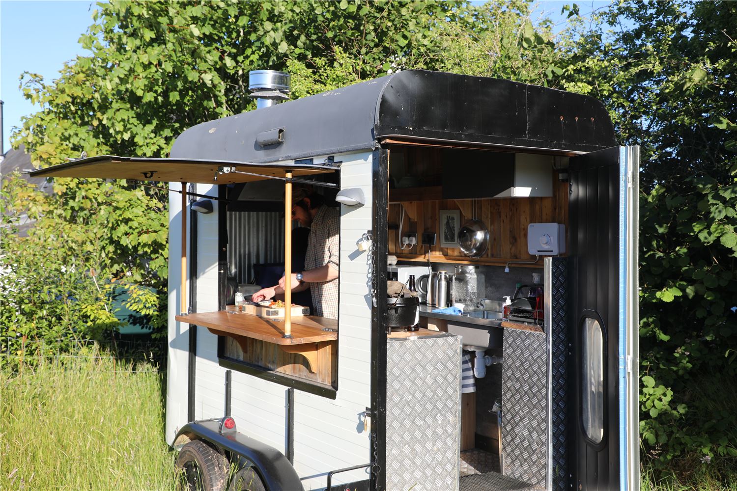 Outdoor kitchen trailer at Farmstead and Wild, showing a compact cooking space with serving hatch, surrounded by trees in rural Bannau Brycheiniog.