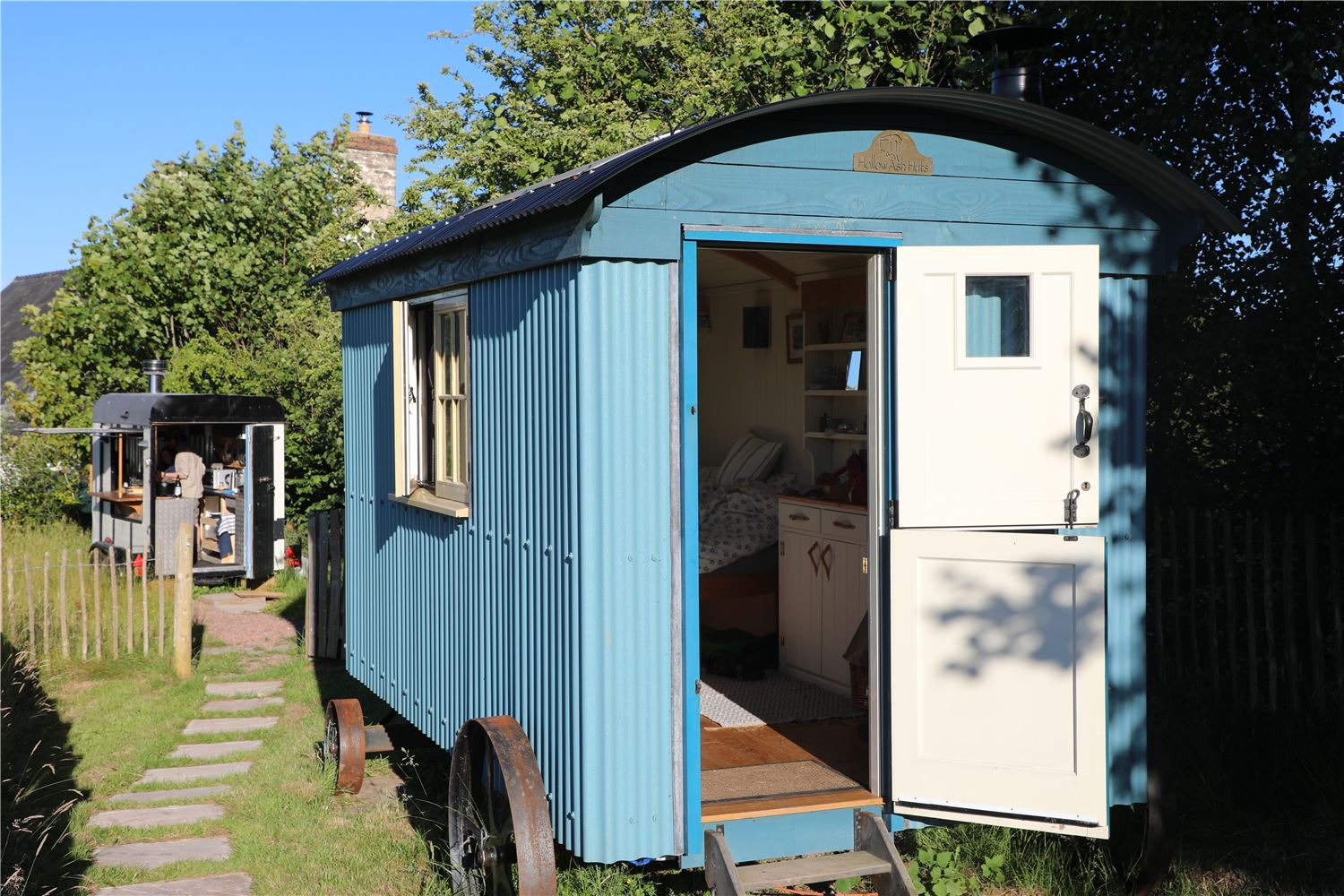 Blue shepherd’s hut at Farmstead and Wild with open door, set on wheels in a peaceful meadow in Bannau Brycheiniog (Brecon Beacons).
