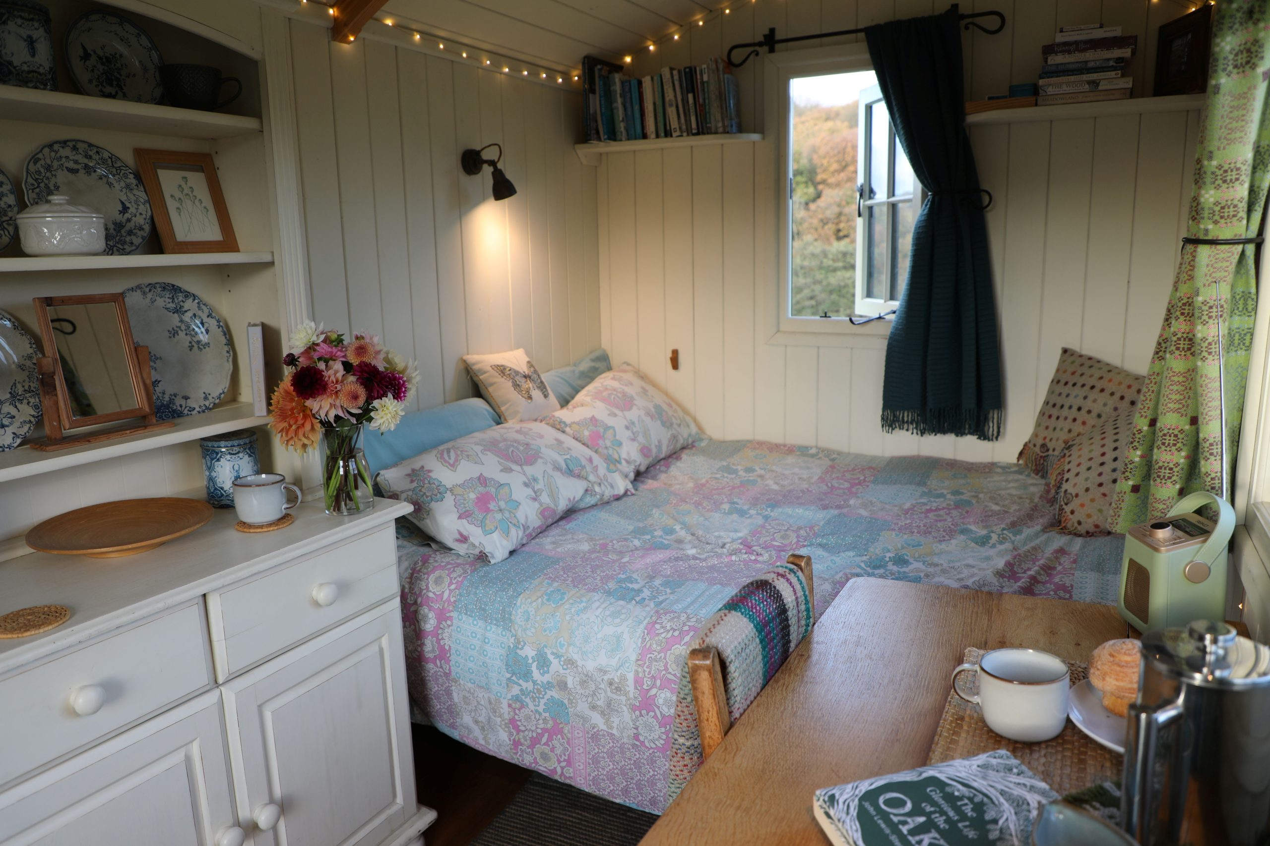 Interior of a shepherd’s hut at Farmstead and Wild, featuring a double bed, wooden furnishings and cosy décor with views over Bannau Brycheiniog.