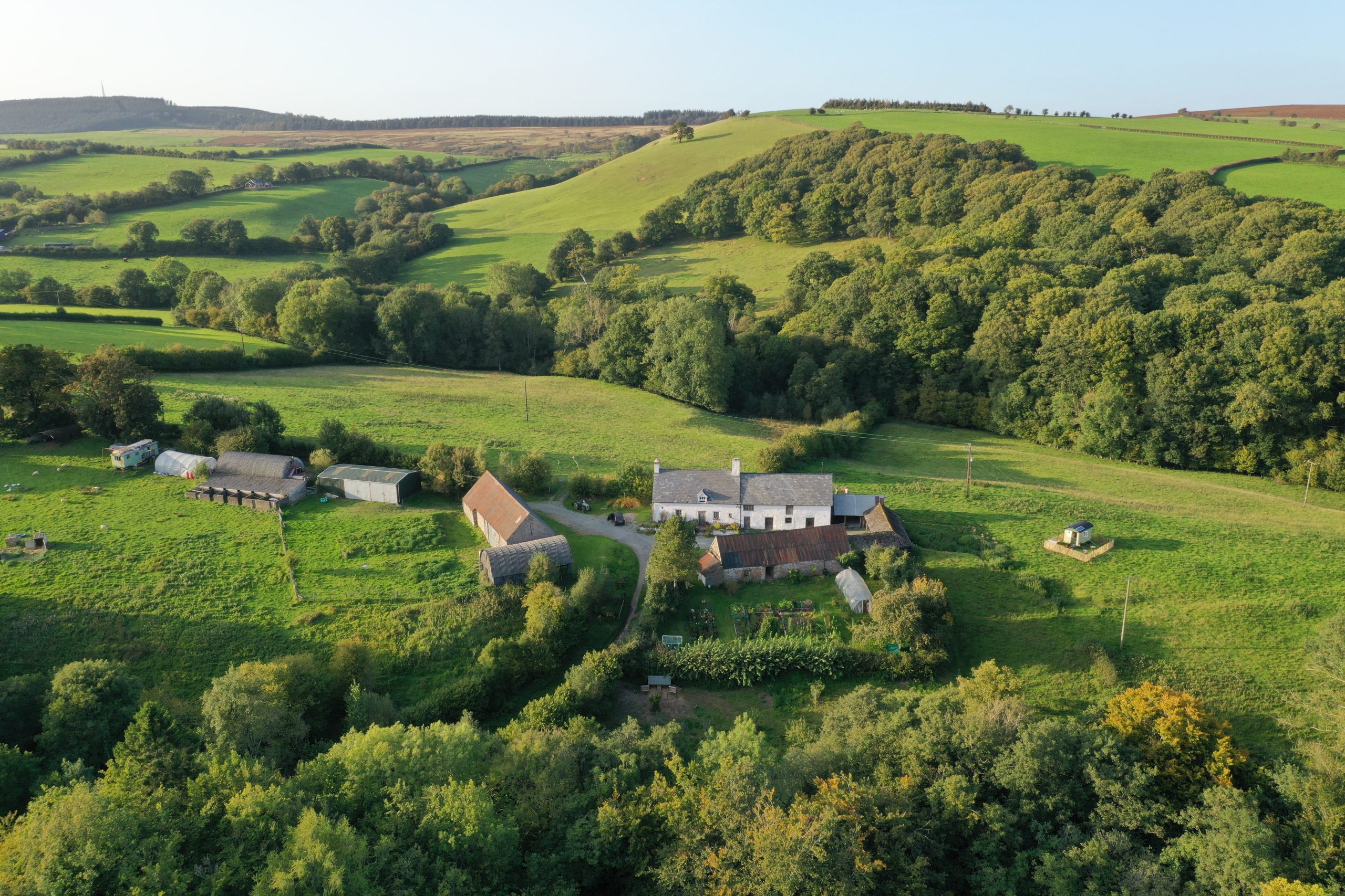 Aerial view of Farmstead and Wild accommodation and surrounding farmland, with rolling green hills and woodland in Bannau Brycheiniog (Brecon Beacons).
