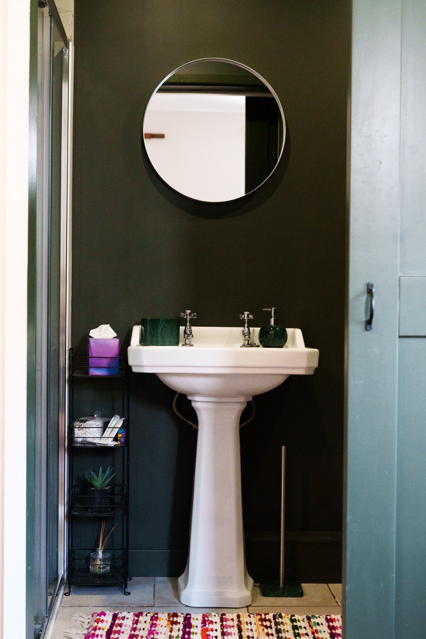 Modern bathroom at Pwll Court Retreat with walk-in shower, pedestal sink and dark green walls.