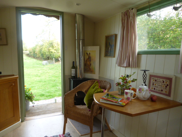 Interior of a cosy shepherd’s hut with wood burner and simple furnishings.