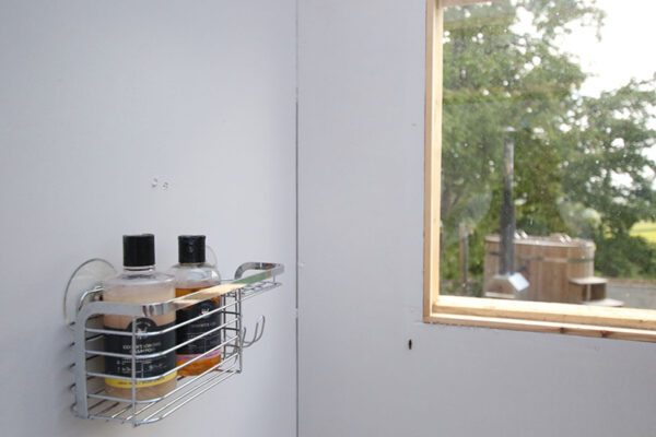 Toiletries in a wall basket beside the washroom window, with Seren Bach’s wooden hot tub visible outside.