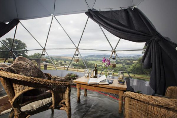 Wicker armchairs and a low table beside the wide triangular-panelled window overlooking countryside in Seren Mawr.