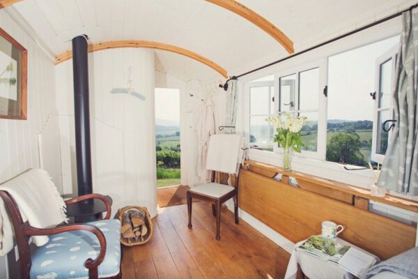 Wood-burning stove, armchair and folding wooden table beneath an open window, with countryside beyond the stable door.