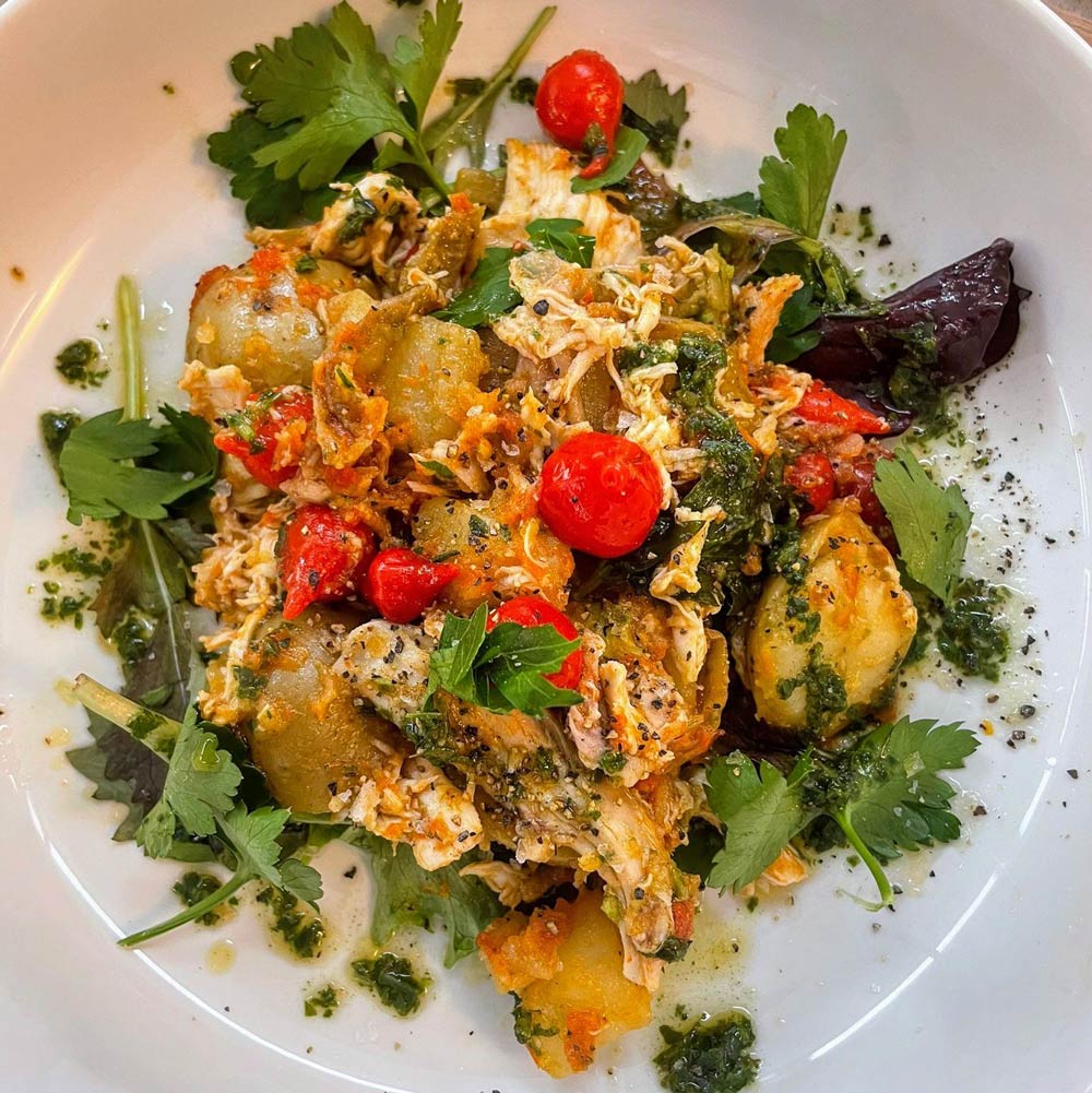 A café dish with cherry tomatoes, leafy herbs and potatoes on a white plate.