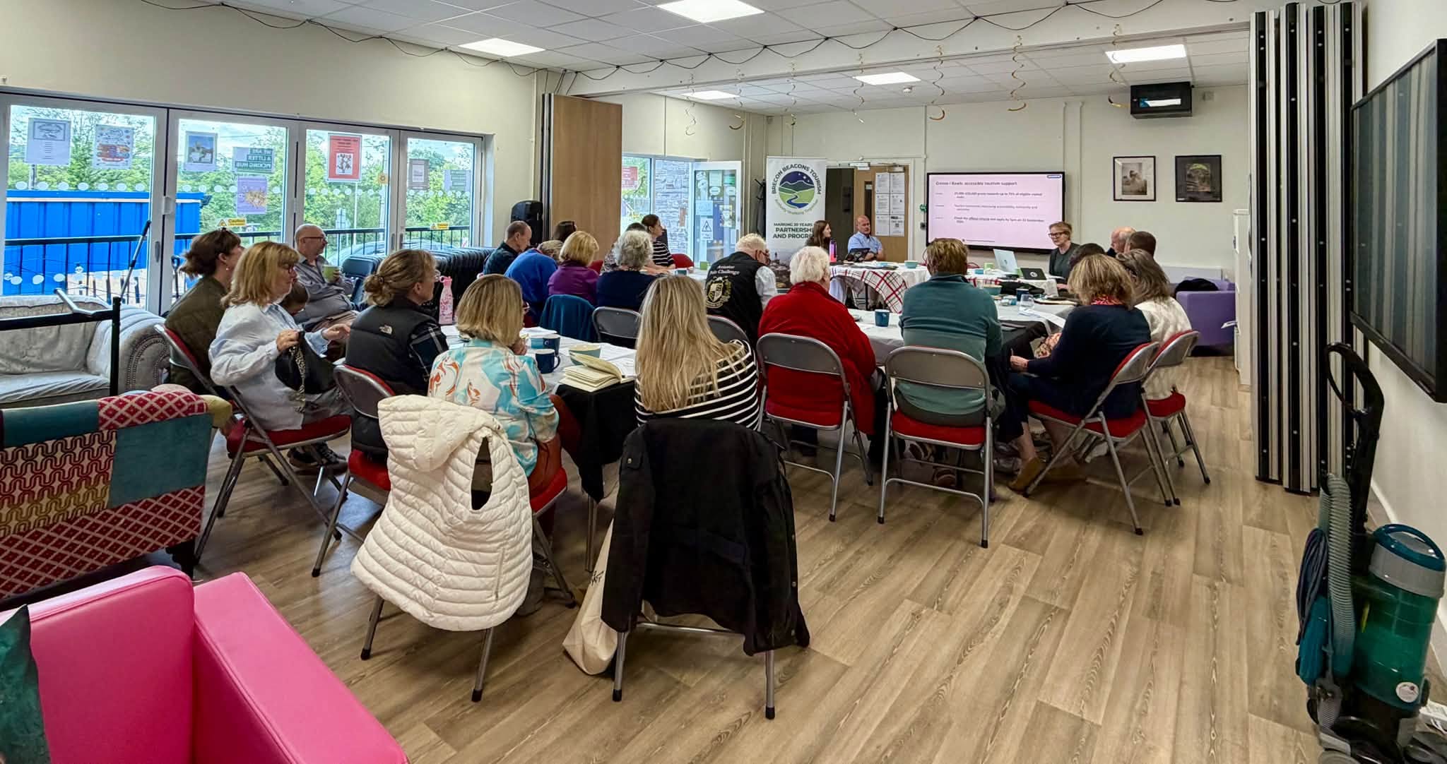 A meeting in the hall at Penderyn Community Centre, with attendees seated around tables