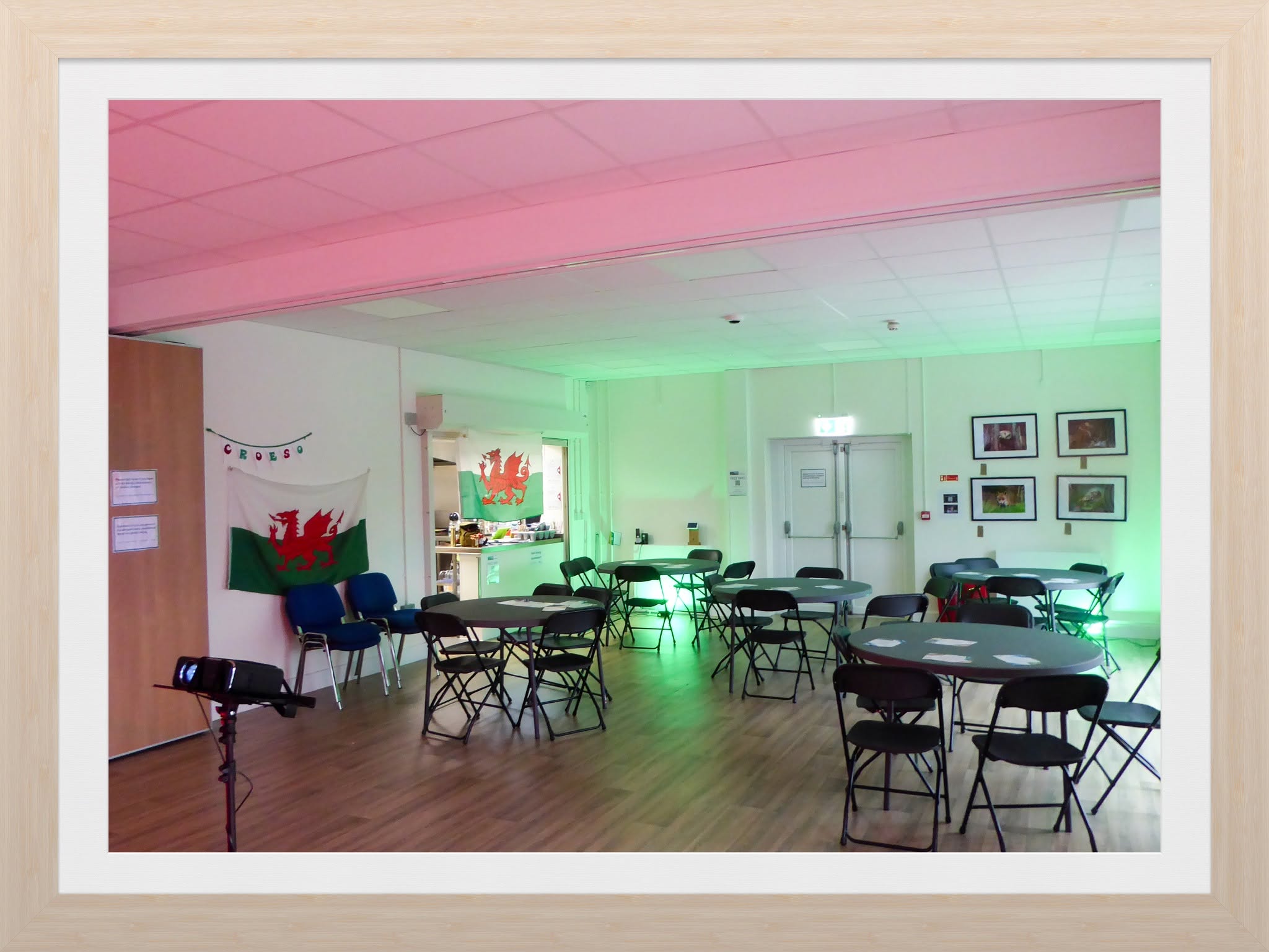 Round tables and chairs arranged for an event at Penderyn Community Centre, with Welsh flags and coloured lighting