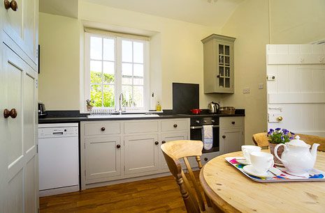 Pale fitted kitchen with a wooden dining table set with a teapot and cups at Garden Cottage