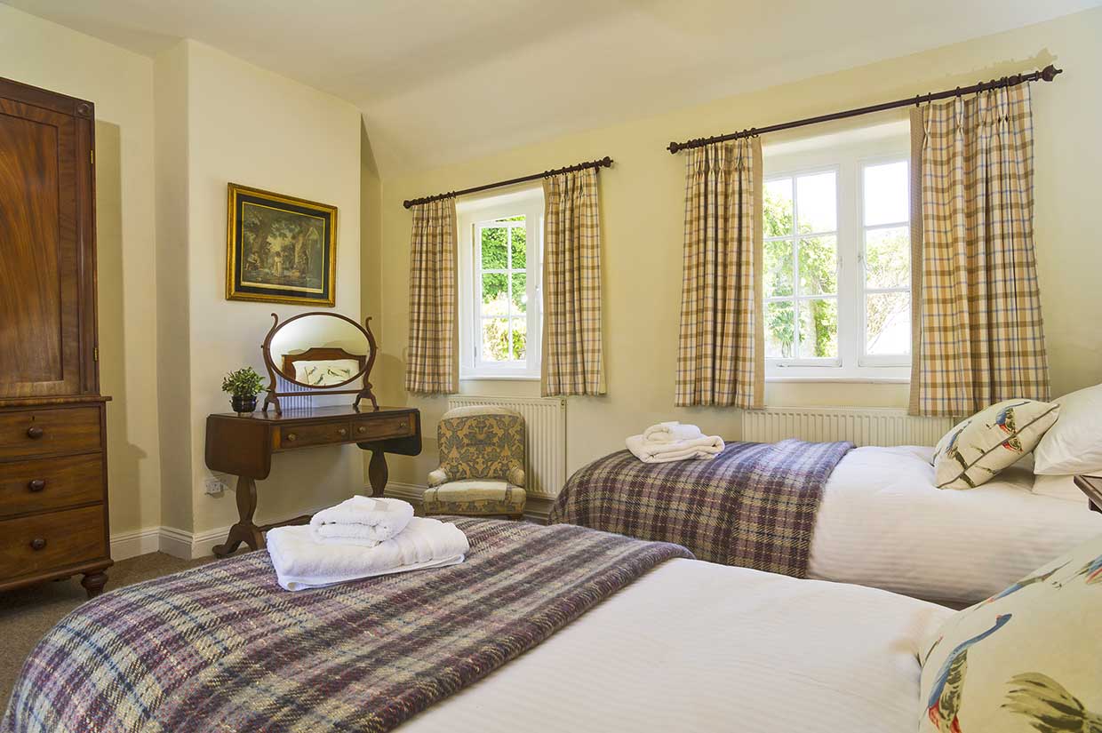 Two single beds with checked blankets and folded towels beside a wooden dressing table at Garden Cottage