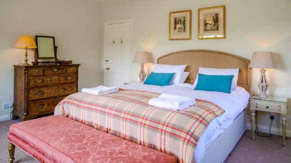 Double bed with a checked throw, turquoise cushions and folded towels at Glanusk Lodge