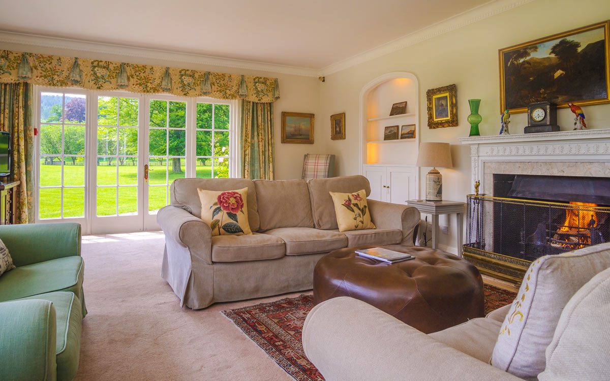 Sofas beside an open fire, with French doors looking onto the lawn at Glanusk Lodge