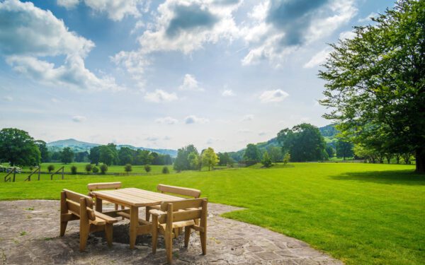 Wooden table and chairs on a paved terrace beside a large lawn with countryside views at Glanusk Lodge