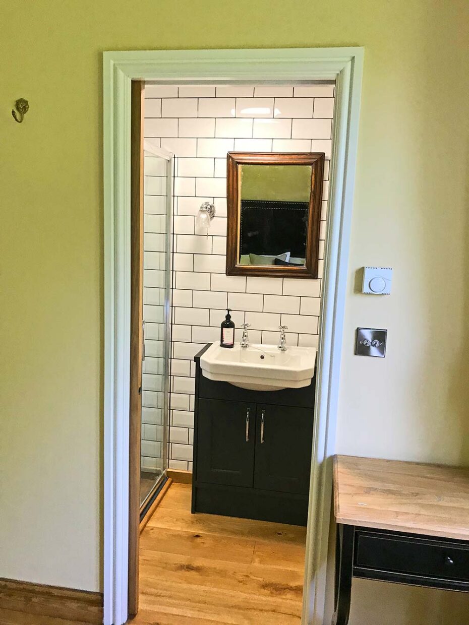 Golygfa drwy ddrws at ystafell gawod en-suite gyda theils gwyn, basn a drych mewn ffrâm yn The Tower