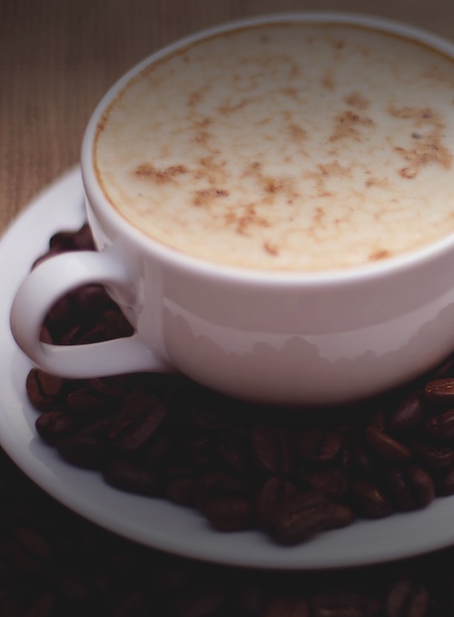 A cup of frothy coffee on a saucer with coffee beans