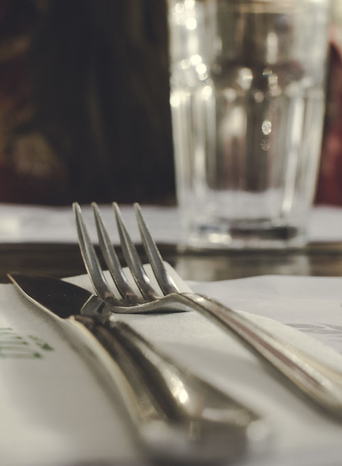 A knife and fork on a folded napkin beside a drinking glass