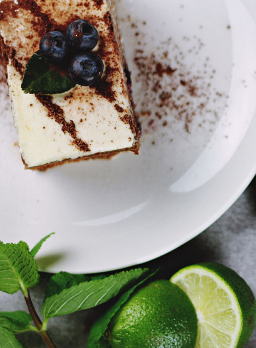 A slice of iced cake topped with blueberries beside mint and lime