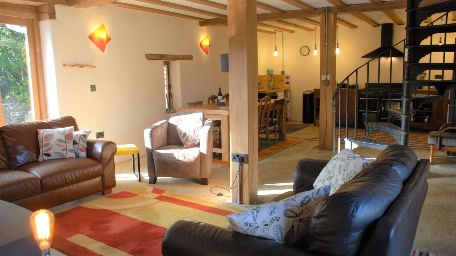 Sofas and an armchair in the Old Barn’s open-plan living room, with timber posts and a spiral staircase.