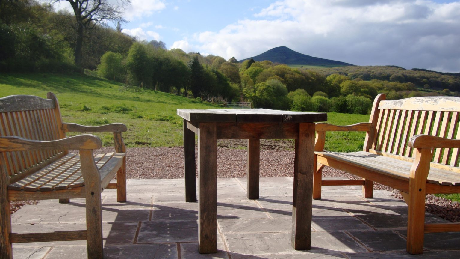 Wooden benches and a table on the Old Barn patio, overlooking green fields and Sugar Loaf.