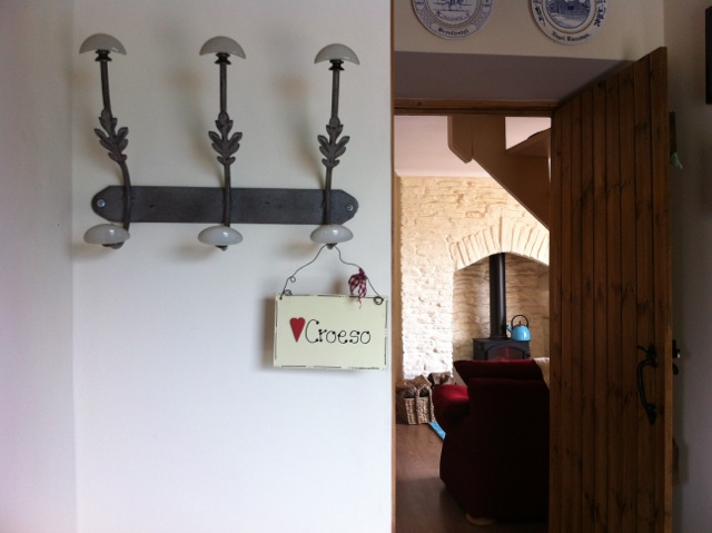 Farm Cottage hallway with coat hooks and an open door towards the lounge at Tan yr Eglwys.