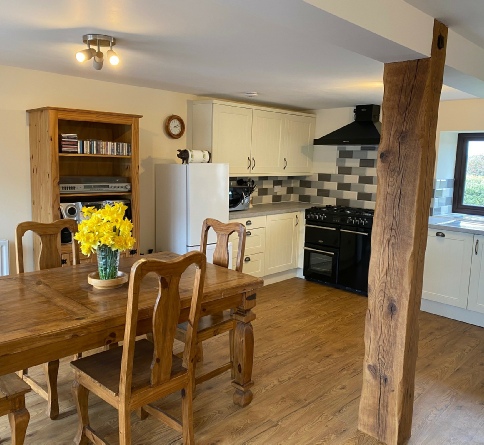 Wooden dining table, exposed timber post and cream kitchen with a black cooker hood in The Granary.