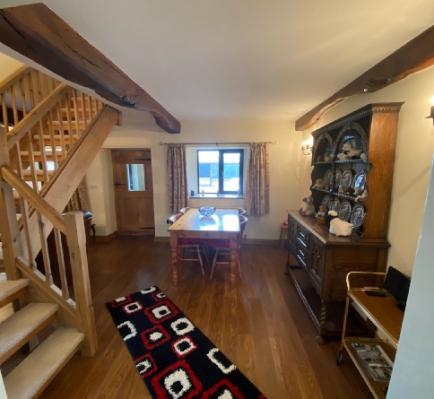 Dining table, wooden dresser and staircase beneath exposed beams in The Stable.