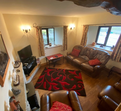 View across The Stable’s living room with brown leather sofas, red cushions and two windows.