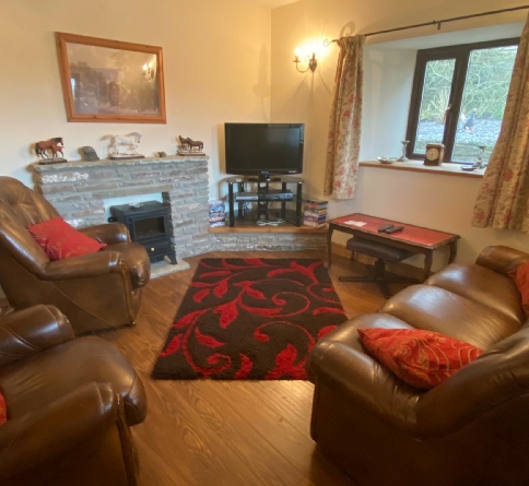 Brown leather seating and a red-patterned rug beside the stone fireplace in The Stable’s living room.