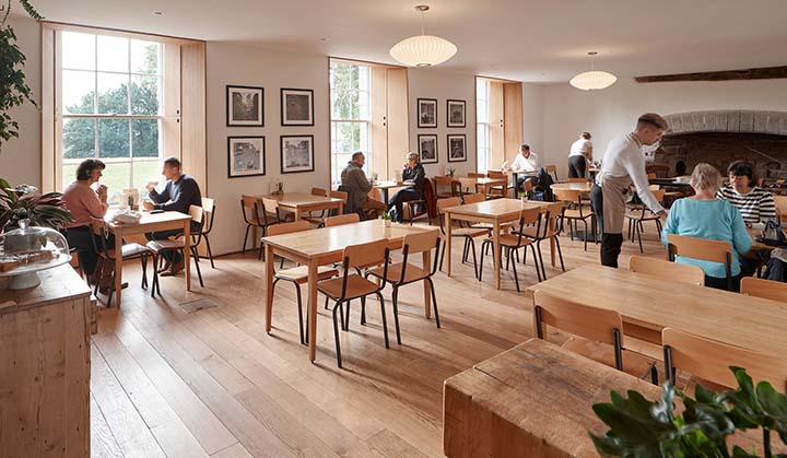 Wooden tables and chairs inside Hay Castle Café, with large windows and a fireplace