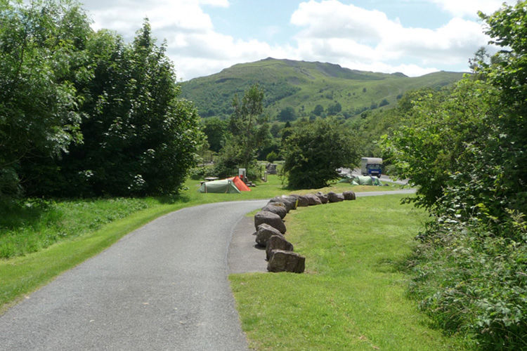 A curving campsite lane beside grassy pitches and tents beneath the mountains at Dan-yr-Ogof.