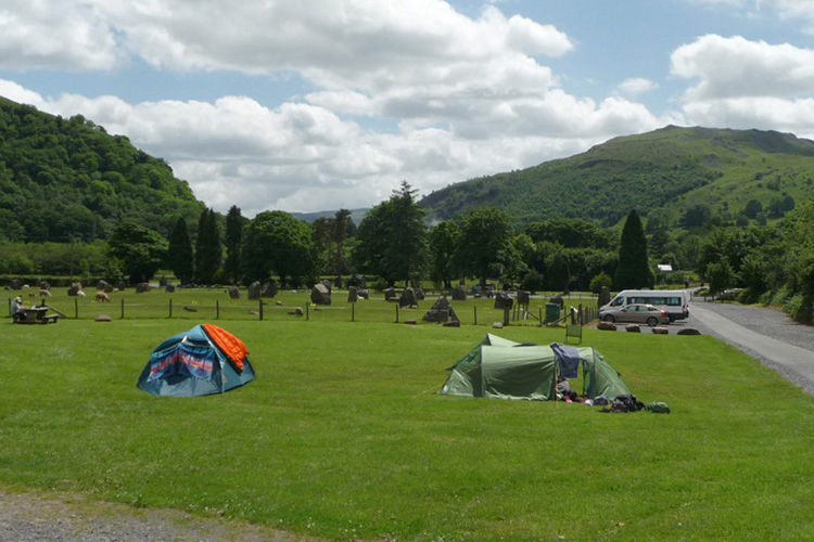 Tents on grass pitches with campervans and mountain scenery at Dan-yr-Ogof.