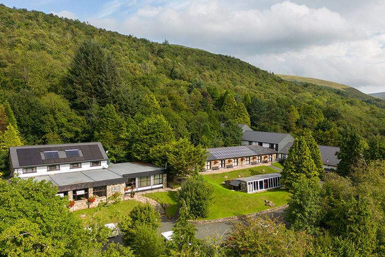 Stone cottages and apartments below a wooded hillside at Brecon Beacons Resort.