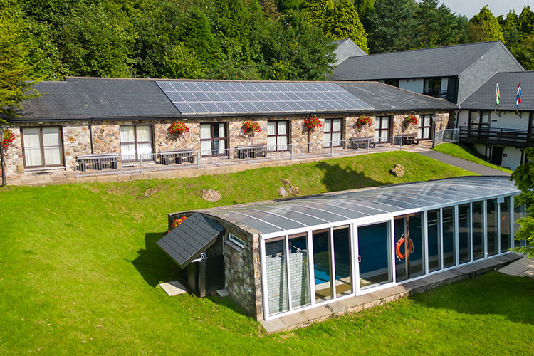 Stone holiday apartments with hanging baskets and solar panels beside the covered pool.